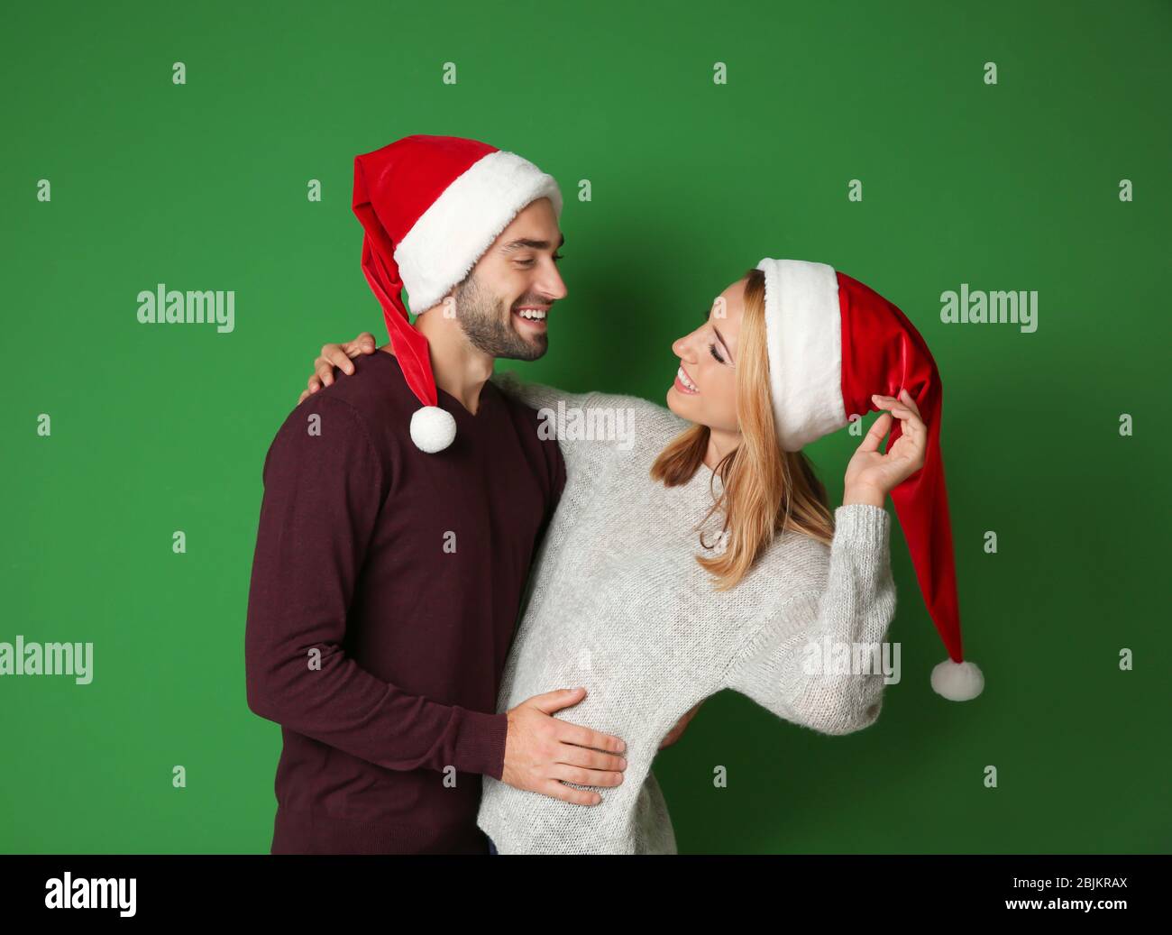 Happy young couple in Santa hats on color background. Christmas concept ...