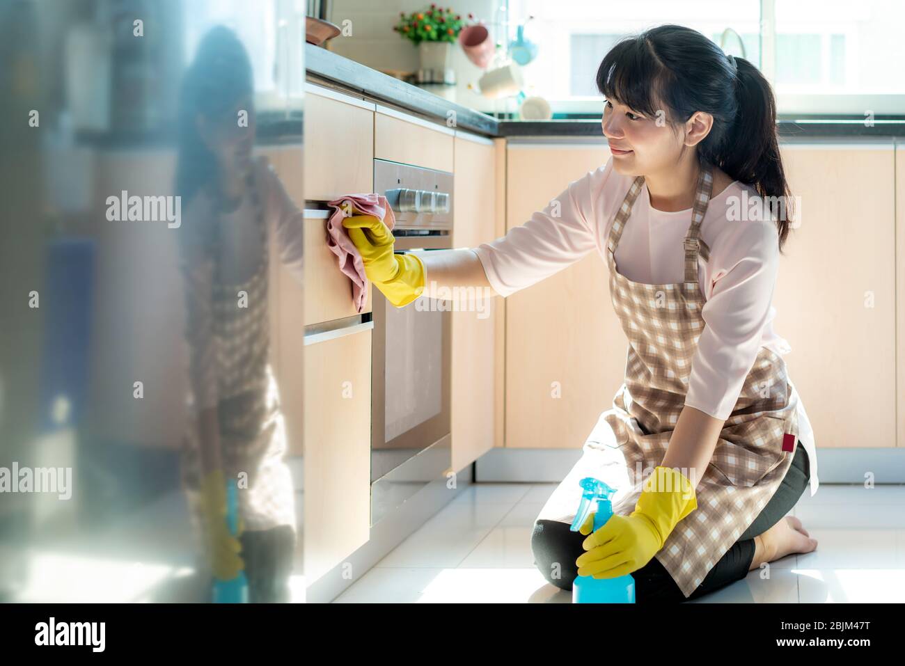 Asian woman wearing rubber protective gloves cleaning kitchen cupboards in her home during Staying at home using free time about their daily housekeep Stock Photo