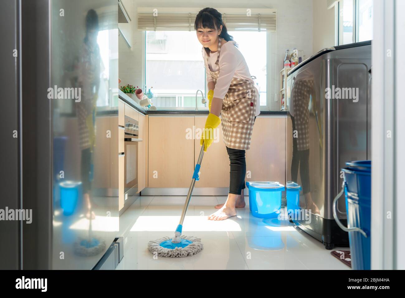 Attractive young Asian woman Mopping the kitchen floor at kitchen while doing cleaning at home during Staying at home using free time about their dail Stock Photo