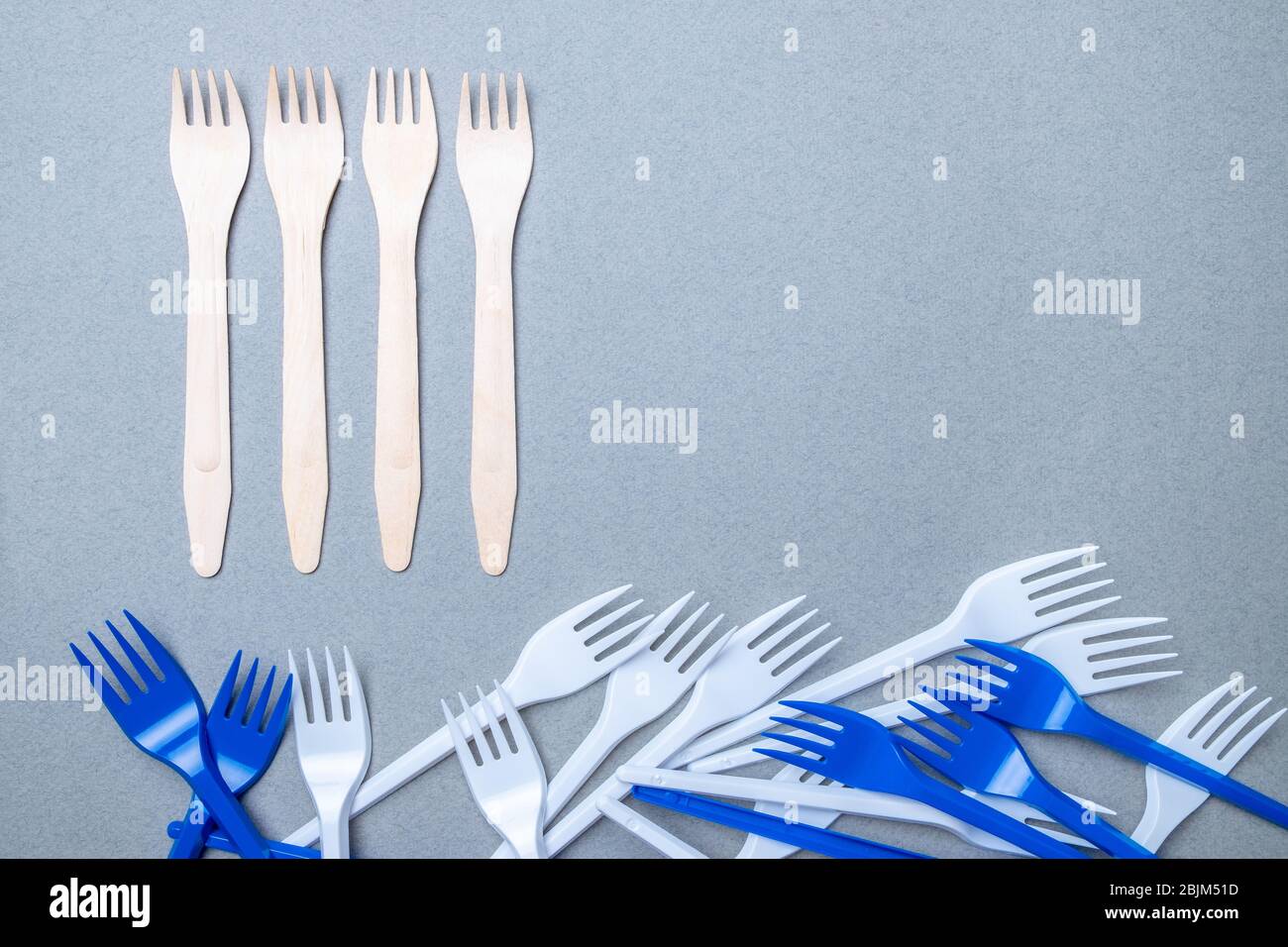 Forks made of wood and plastic on a gray background. Flat lay. Copy space. The concept of environmental pollution by difficult decomposable waste. Stock Photo