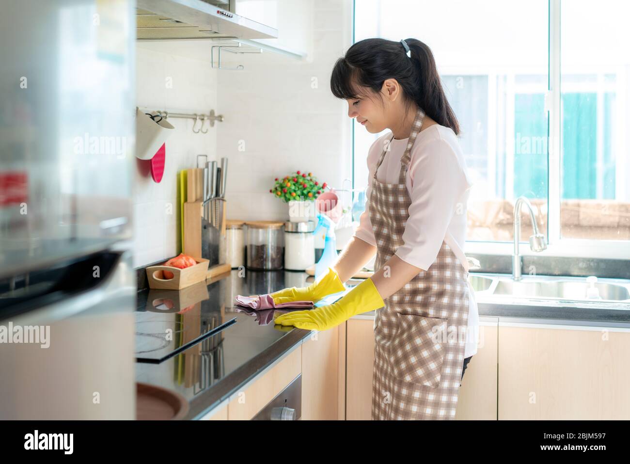 Asian woman wearing rubber protective gloves cleaning kitchen cupboards in her home during Staying at home using free time about their daily housekeep Stock Photo