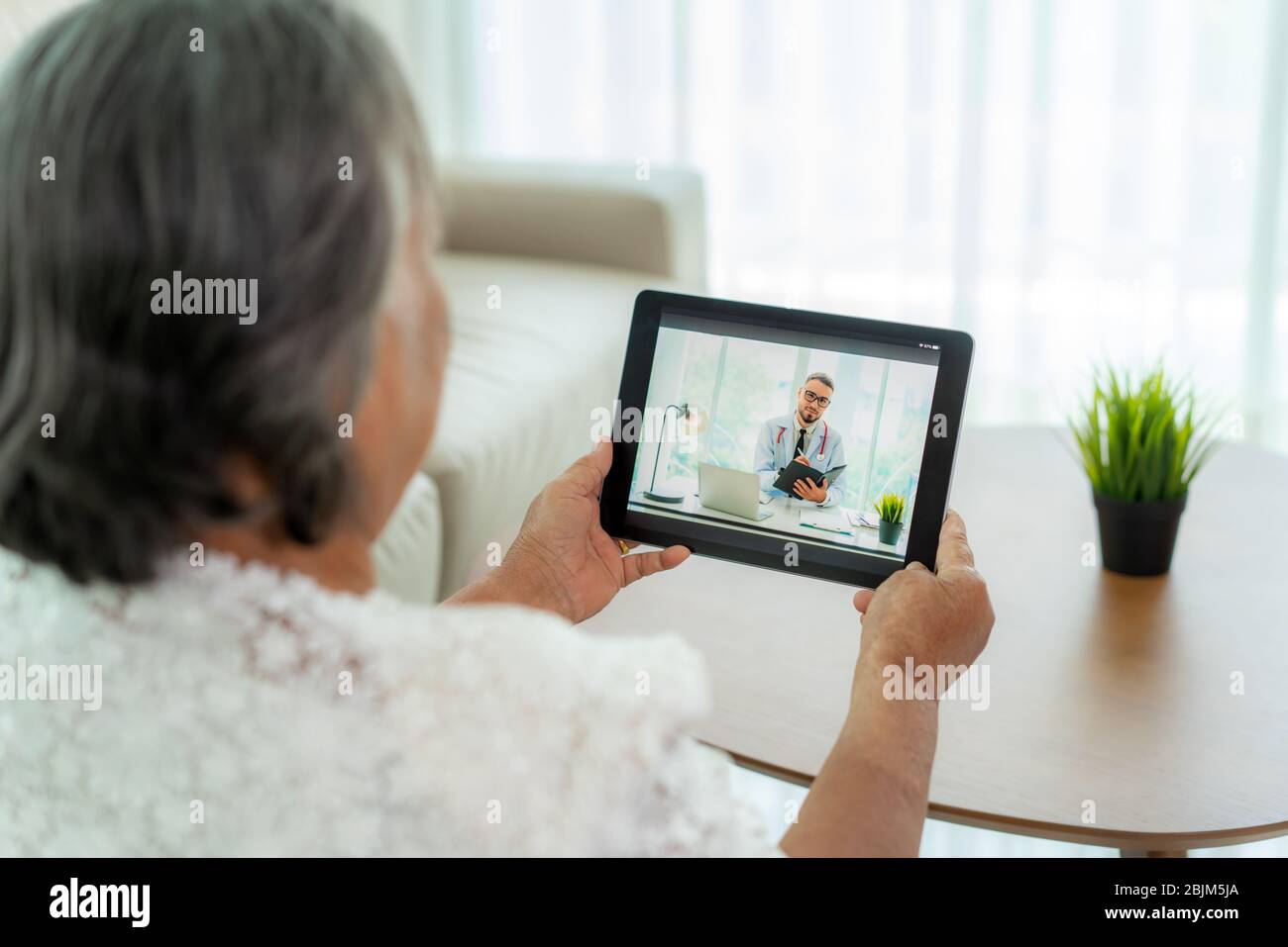 Back view of elderly woman making video call with her doctor with her feeling sick on digital tablet online healthcare digital technology service cons Stock Photo