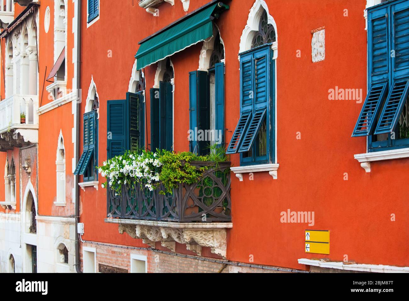 Bold and vibrant orange painted exterior wall with black wooden shutters and white trim of an old Italian home in Venice, Italy. Metal balcony covered Stock Photo