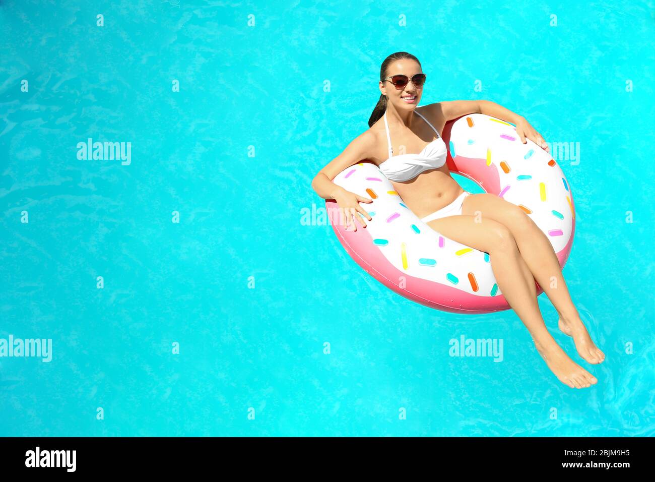 Young woman relaxing on inflatable donut in swimming pool Stock Photo