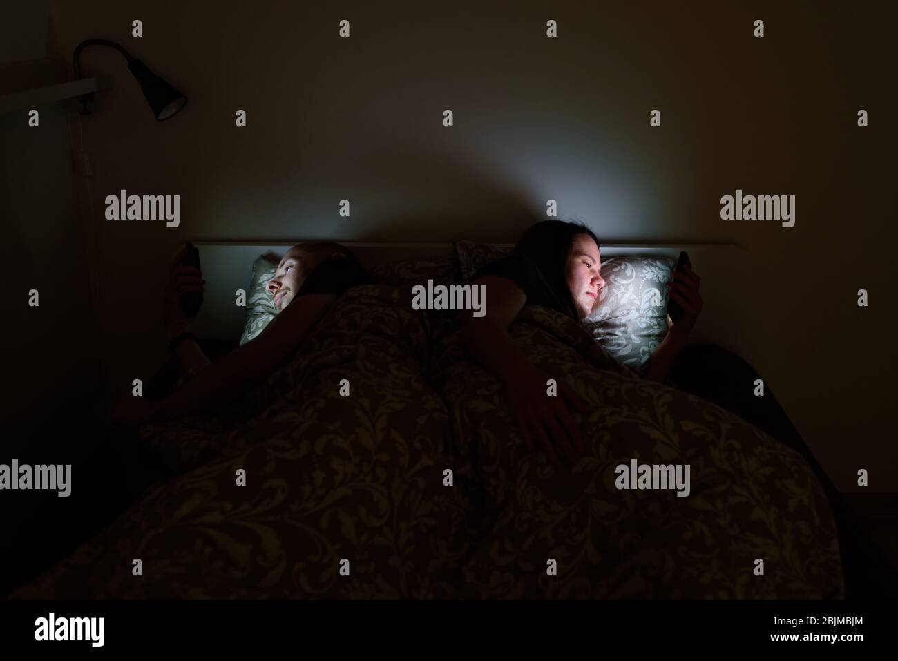Couple using phones lying in bed before sleep. Blue screen light, sleep