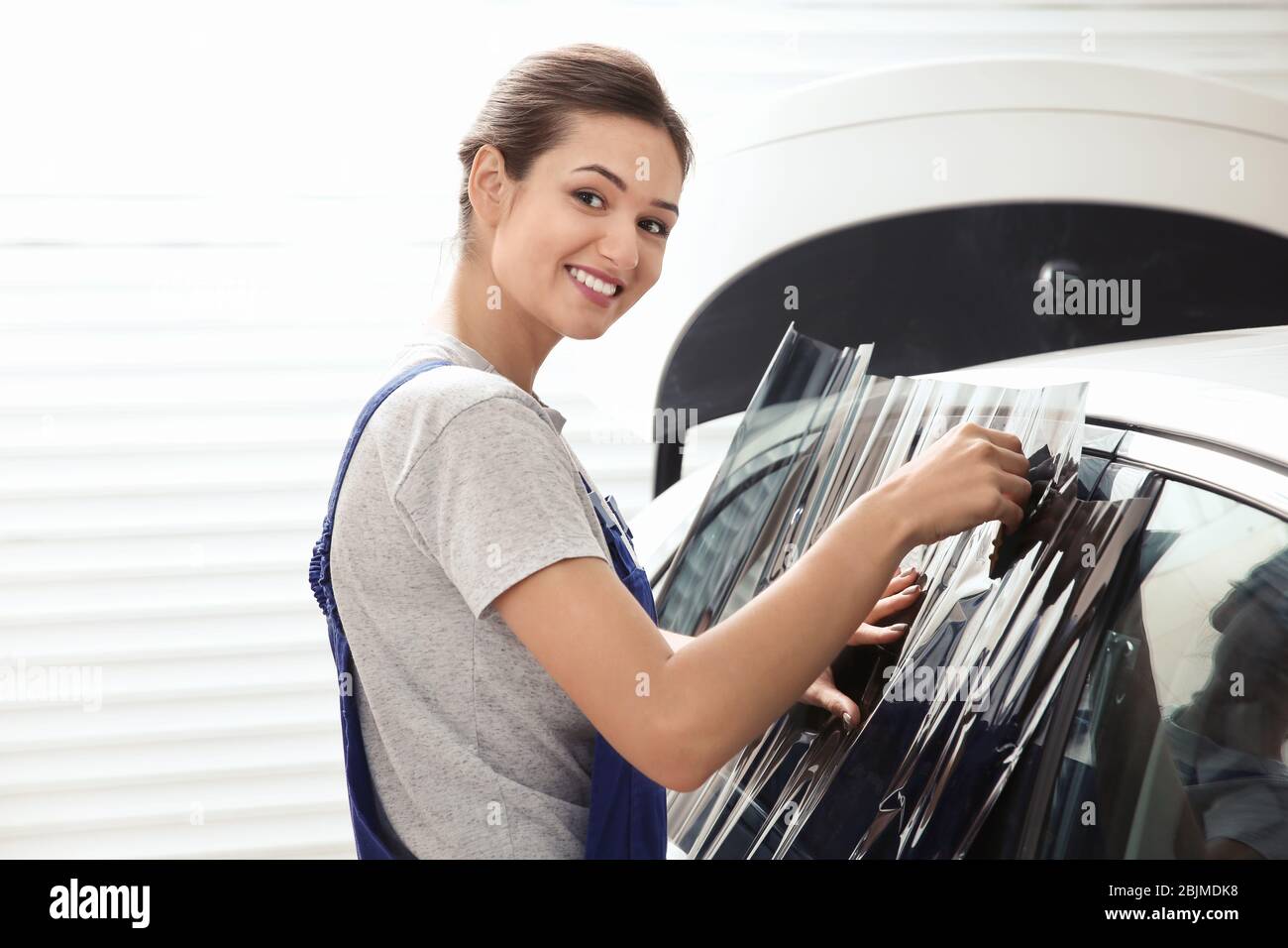 Female worker applying tinting foil onto car window in shop Stock Photo