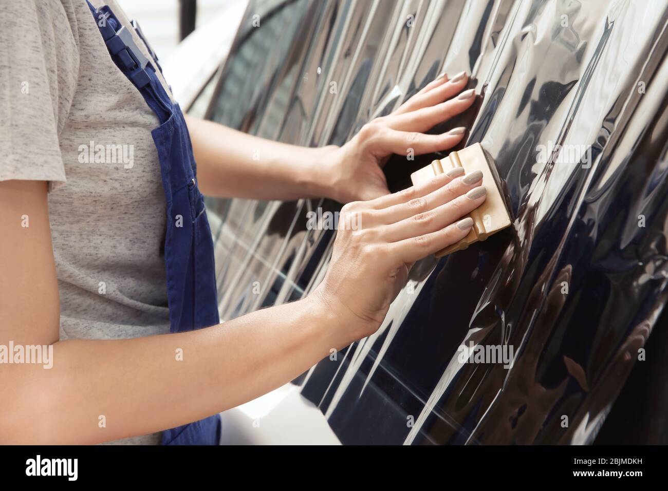 Female worker applying tinting foil onto car window in shop Stock Photo