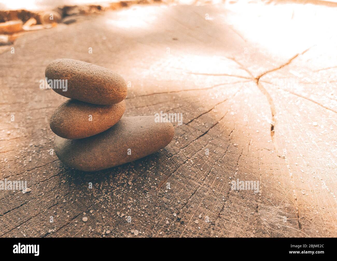 Yoga Zen stones balance on top of each other. Sea pebbles lies on a wooden saw lit by the sun. Copy space. Stock Photo