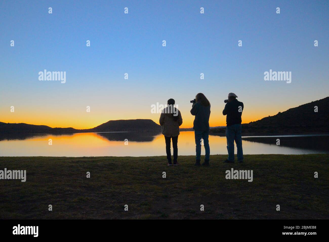 South African outdoor photos by Friedrich von Horsten. Three photographers silhouetted against a dam at sunset Stock Photo