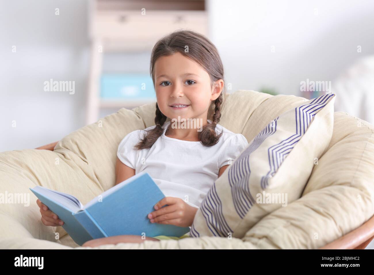 Cute little girl reading book at home Stock Photo - Alamy