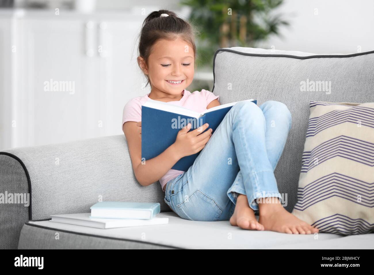 Cute little girl reading book at home Stock Photo - Alamy