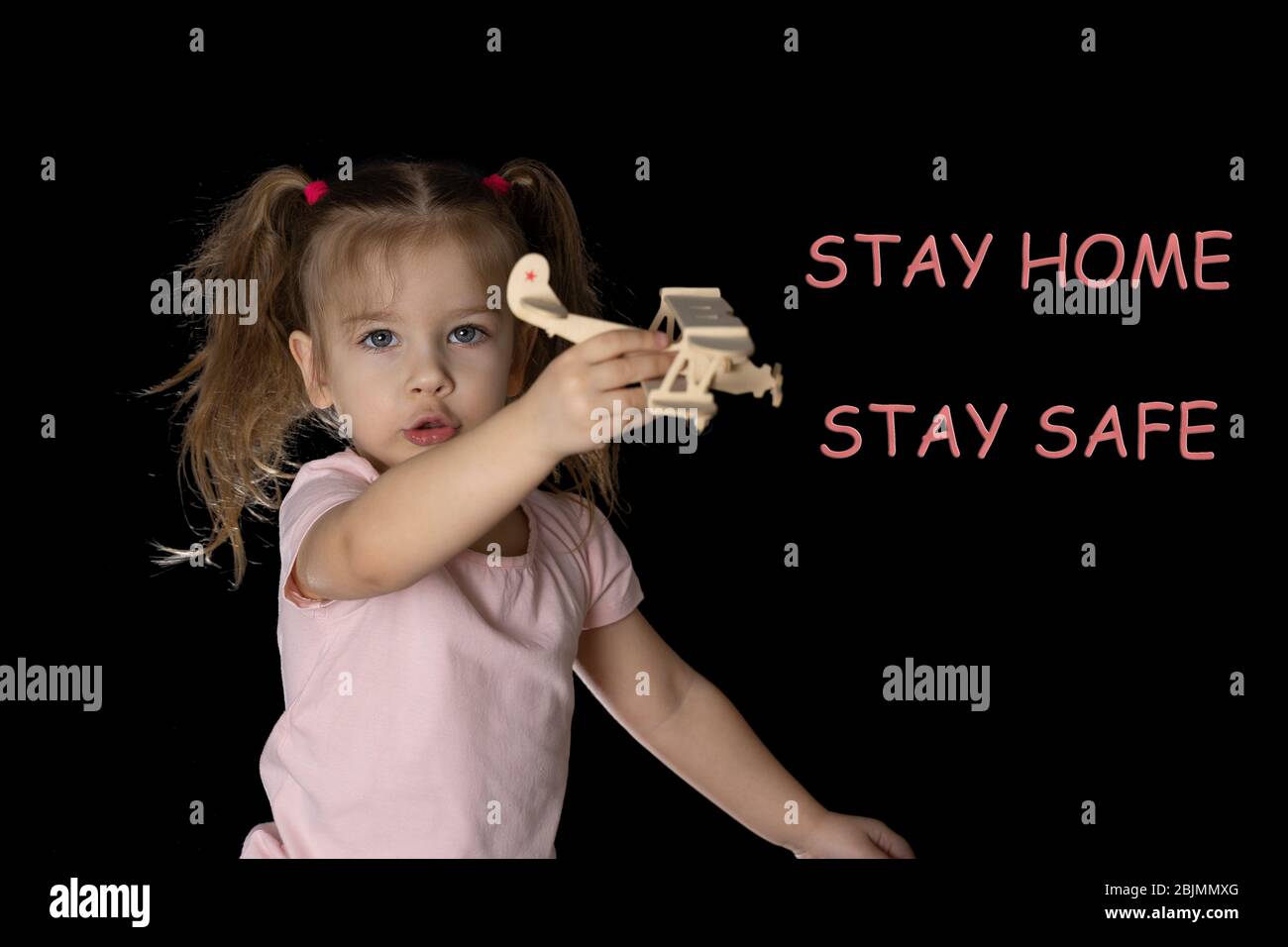 stay home save life text on dark background. sitting next to the floor is a little girl in jeans and playing with a wooden airplane. the need to stay Stock Photo