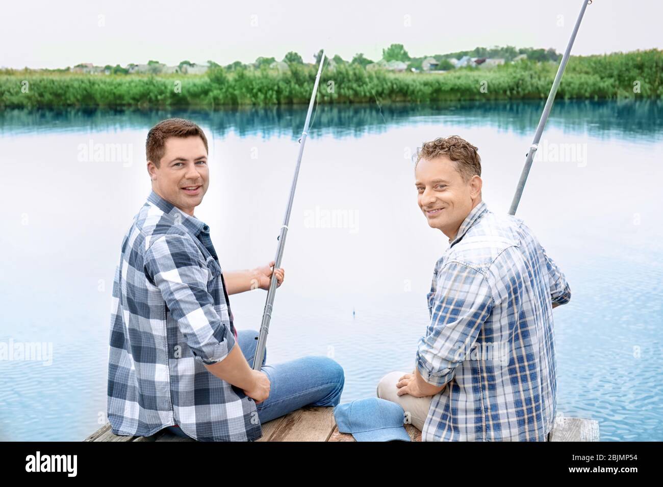 Two men fishing from pier on river Stock Photo - Alamy