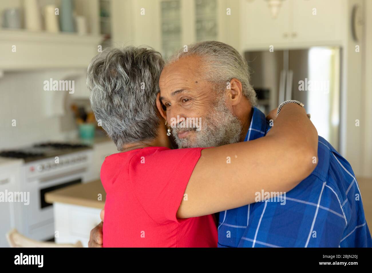 Happy senior couple hugging each other in their kitchen Stock Photo