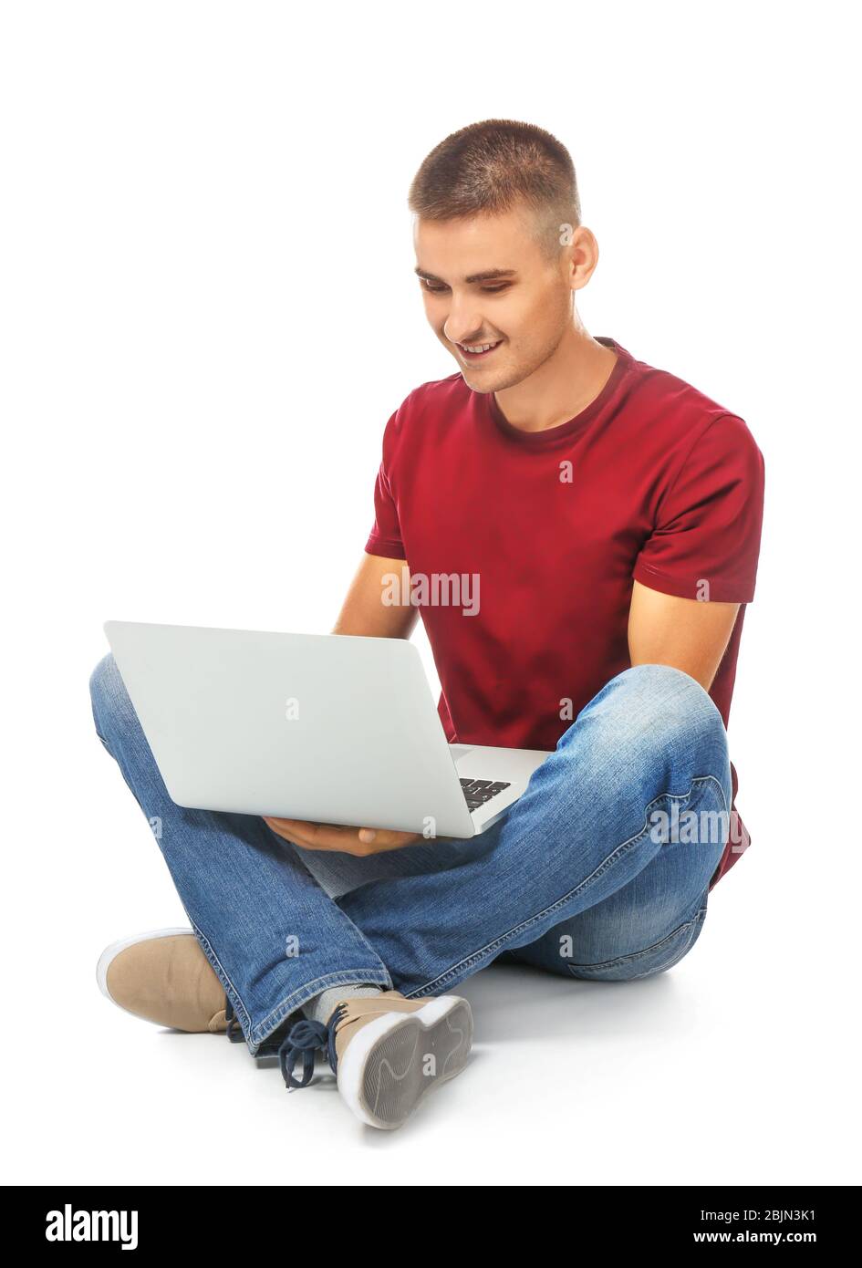 Handsome young man sitting and using laptop against white background ...