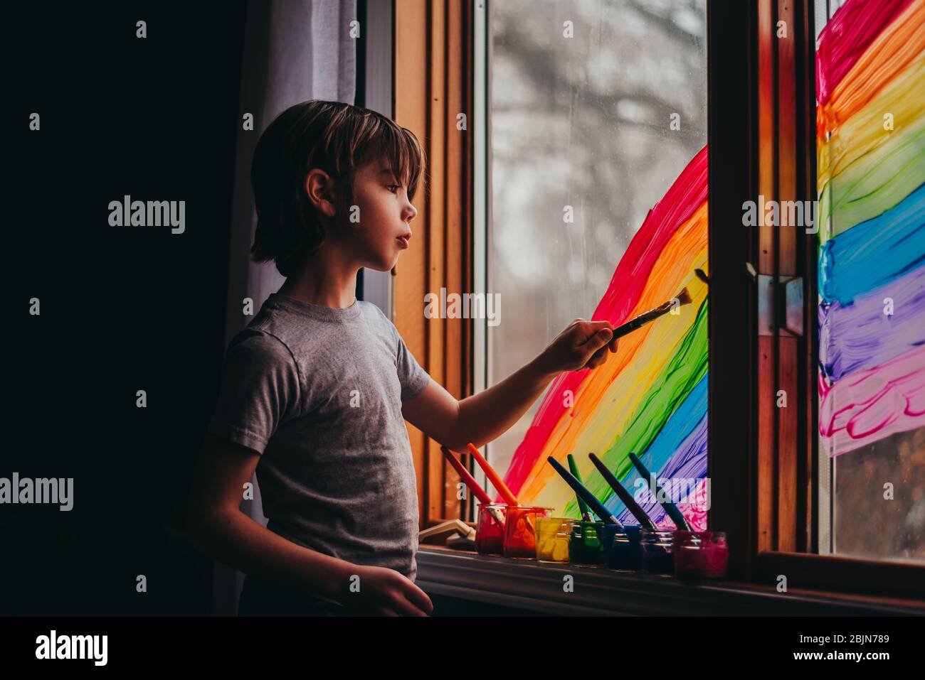 Boy painting a rainbow on a window, USA Stock Photo