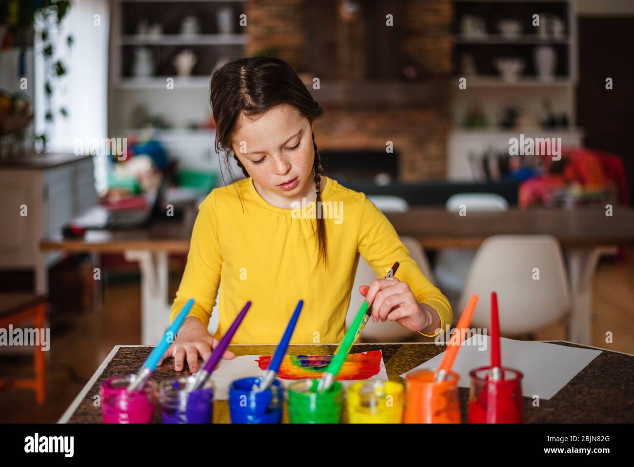 Girl sitting in the kitchen painting a rainbow Stock Photo