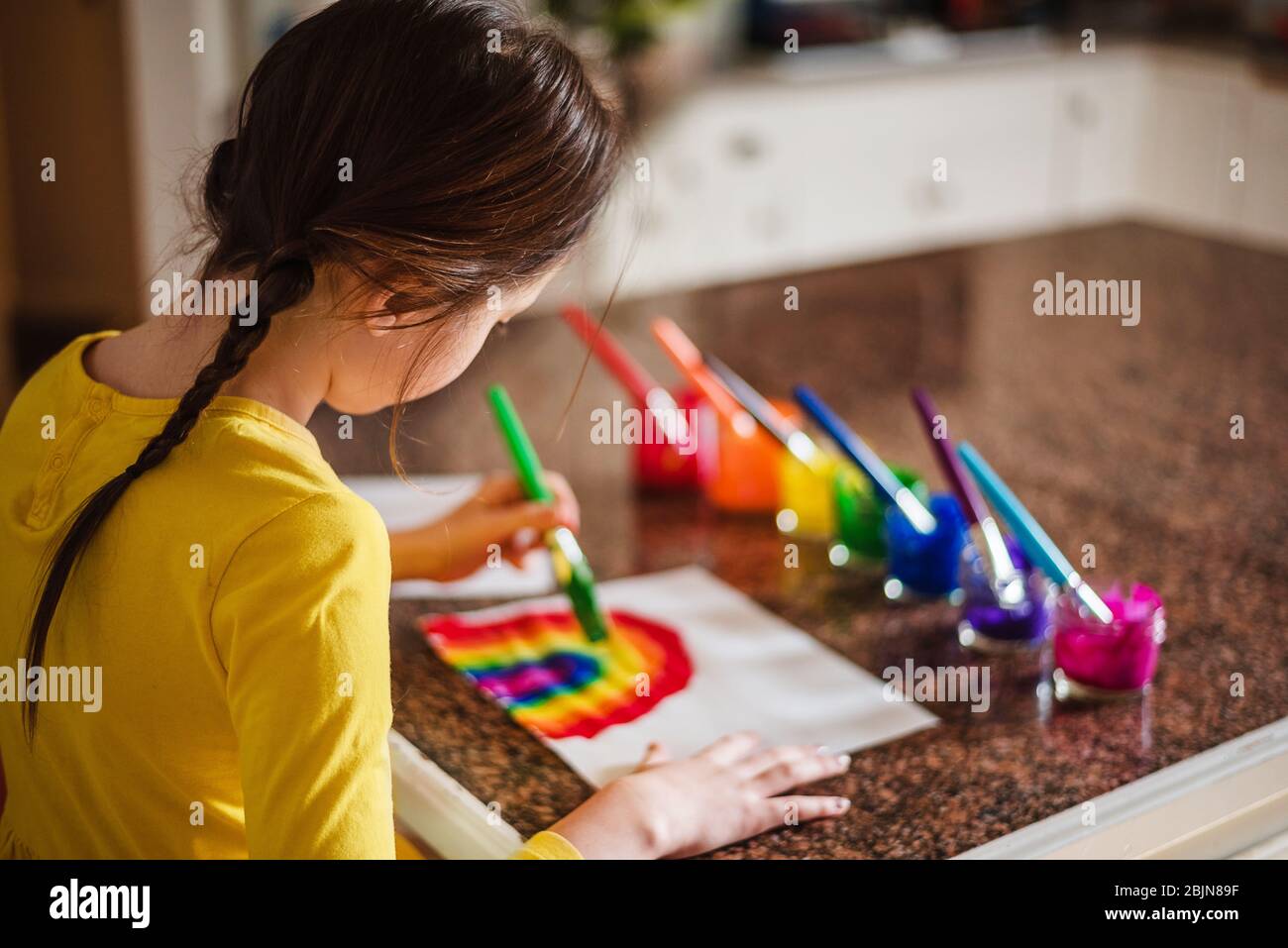 Girl sitting in the kitchen painting a rainbow Stock Photo