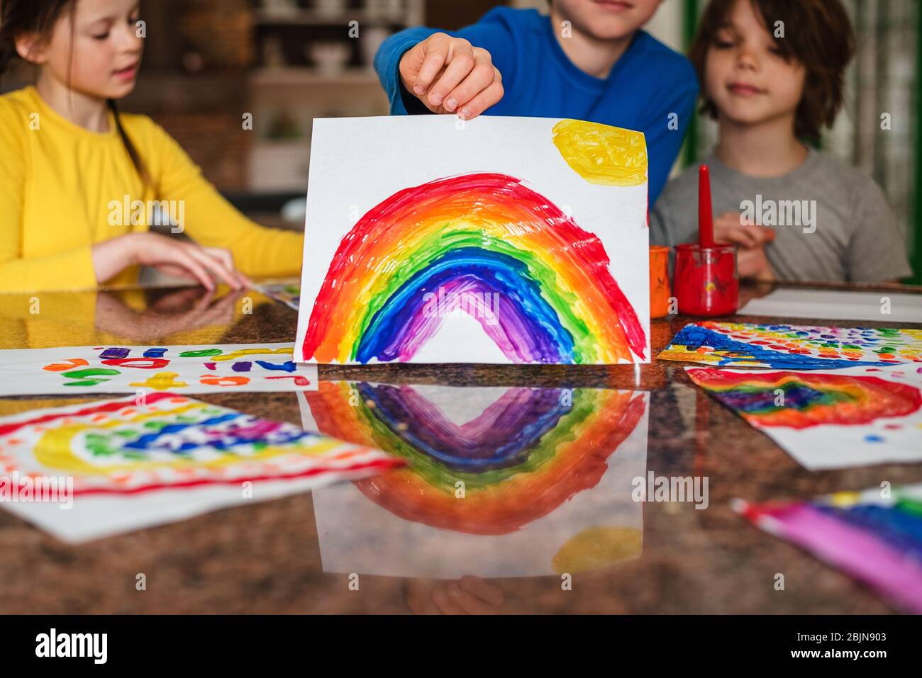 Three children sitting in the kitchen painting a rainbow Stock Photo