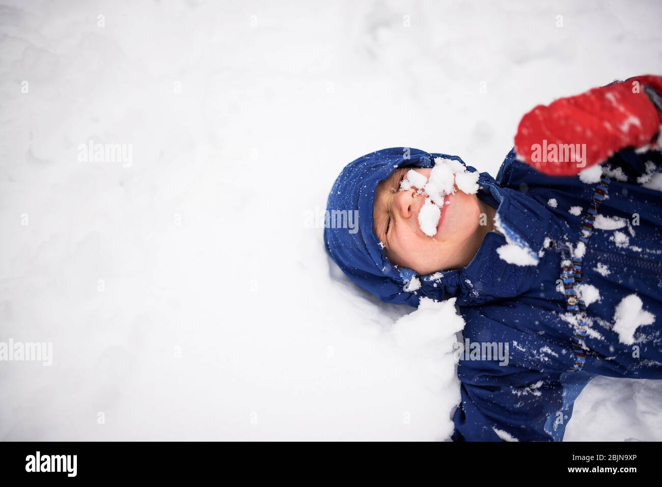 Happy boy lying on the ground covered in snow, USA Stock Photo