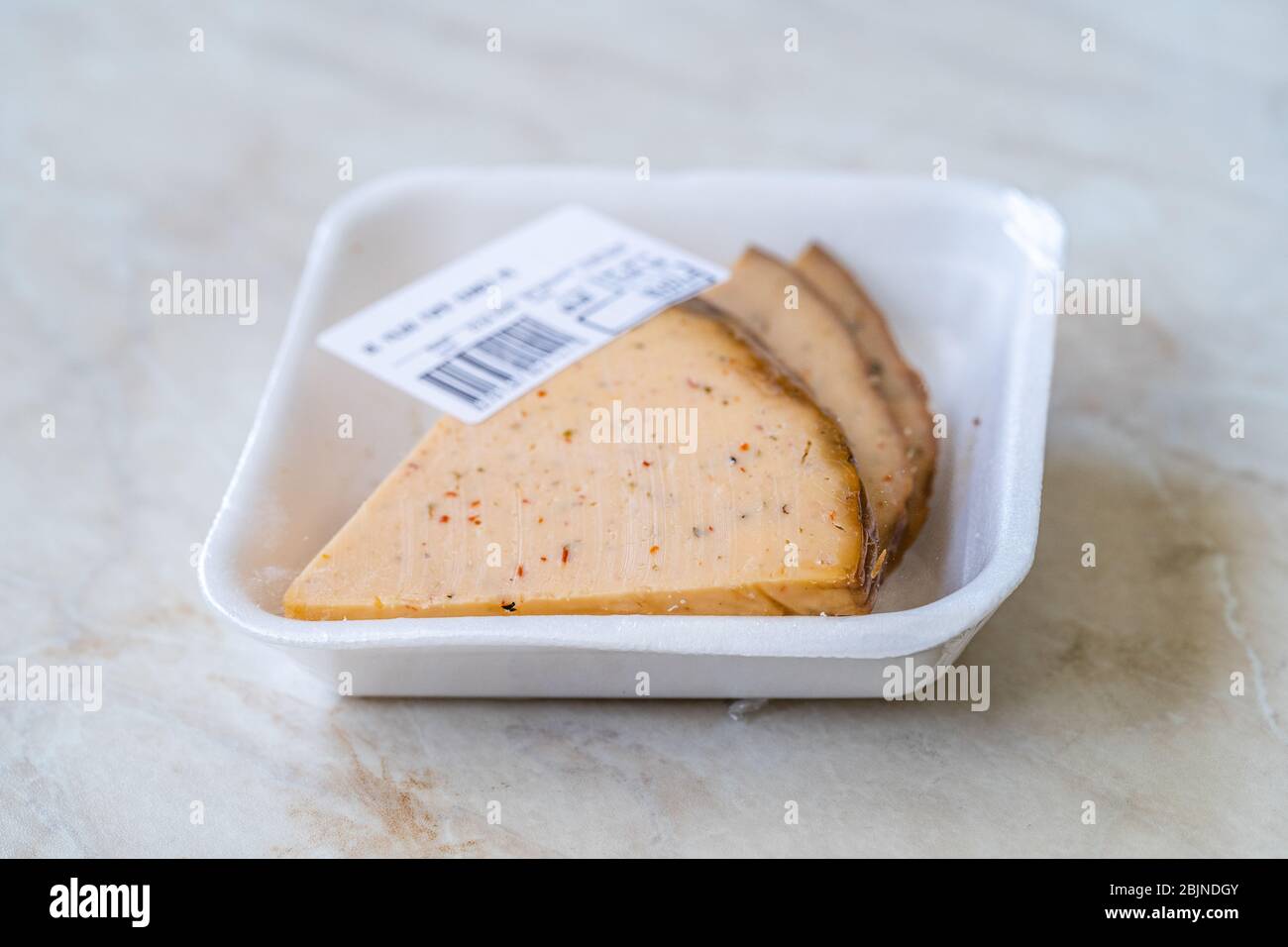 Spicy Circassian Triangle Smoked Cheese Slices on Dark Wooden Plate with Spices for Sale in Plastic Container Package Box. Ready to Eat. Stock Photo