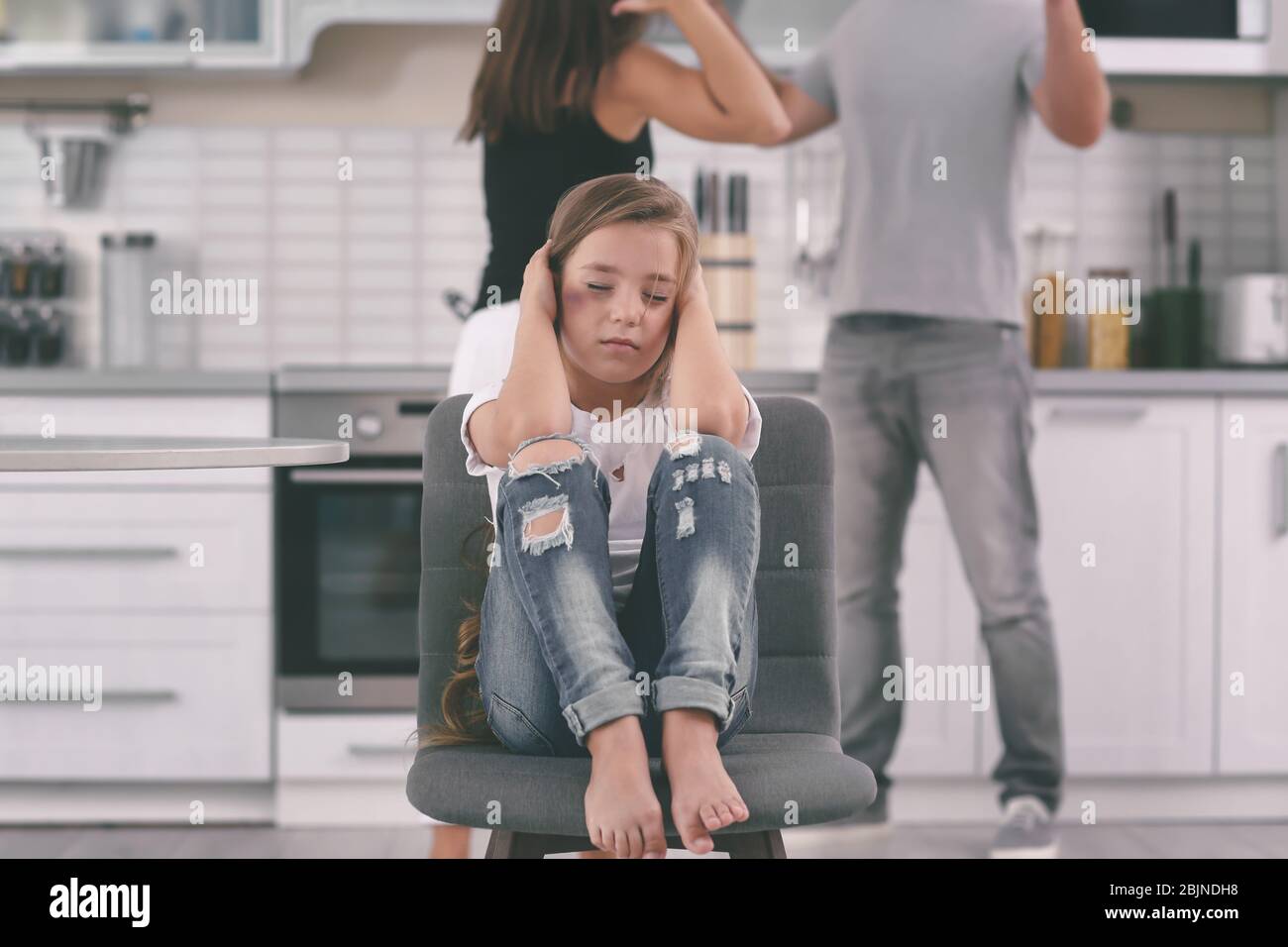 Little girl with bruise covering ears while her parents fighting on background. Domestic violence concept Stock Photo