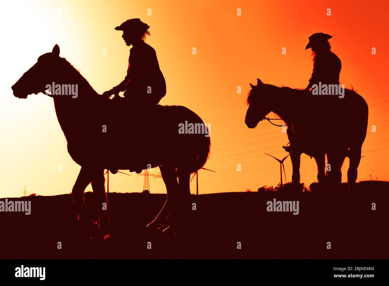 Young people riding horses at sunset time - Silhouette Horseback travel people having fun exploring wild nature Stock Photo