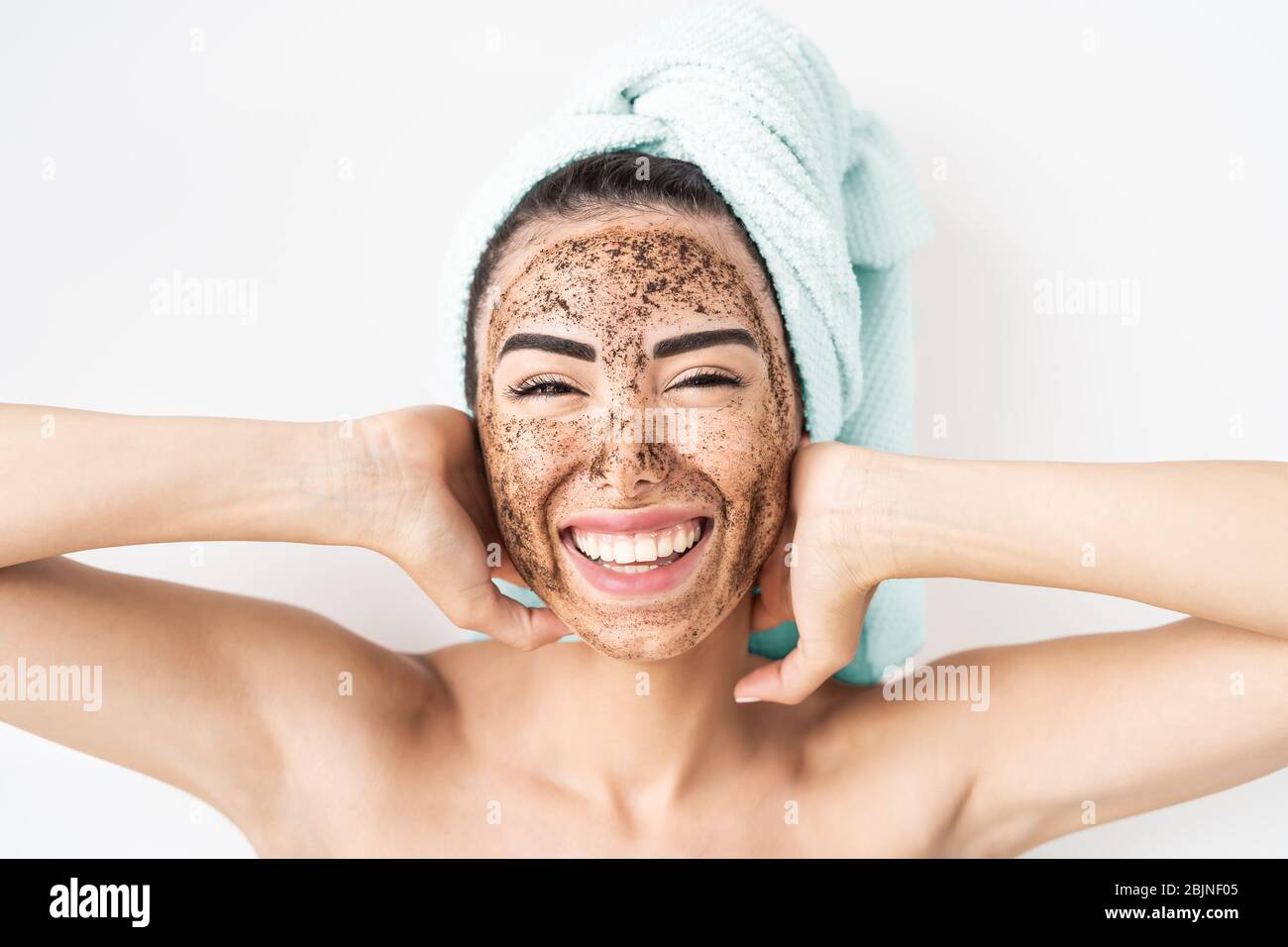 Young smiling woman applying coffee scrub mask on face - Happy girl having skin care spa day at home Stock Photo