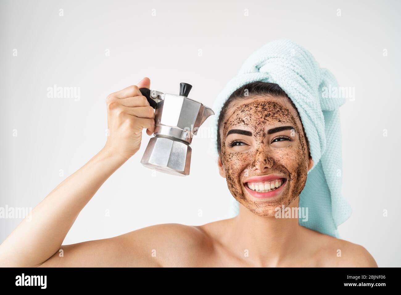 Young smiling woman applying coffee scrub mask on face - Happy girl having healthy skin care spa day at home Stock Photo