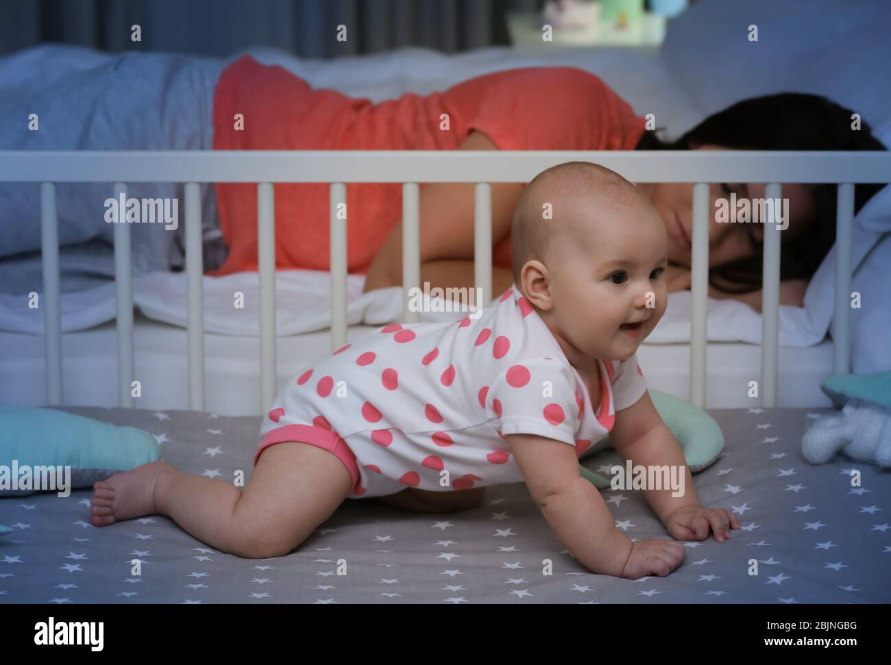 Cute awaken baby near sleeping mother at home Stock Photo