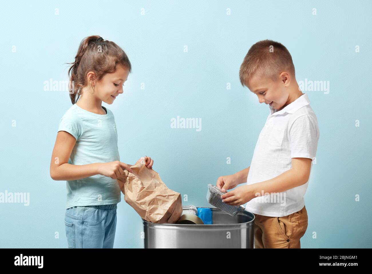 Little children throwing garbage into litter bin on color background. Recycling concept Stock