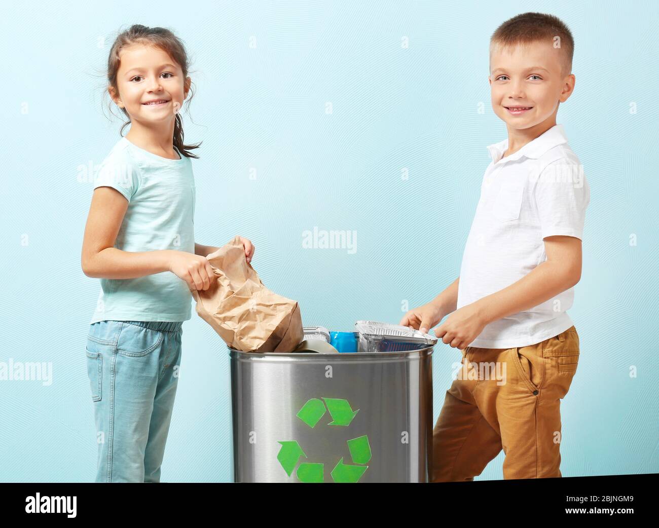 Little children throwing garbage into litter bin on color background