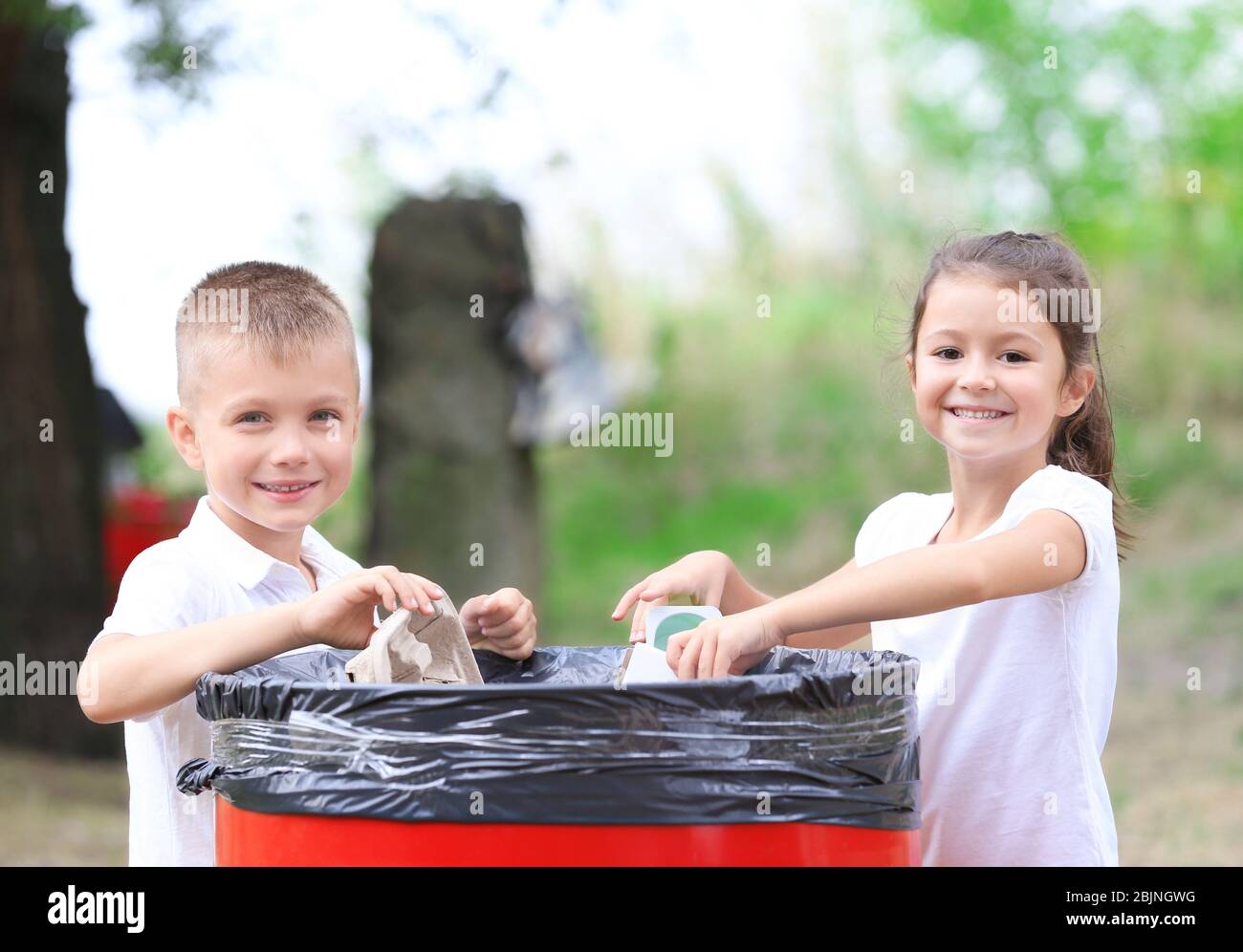Little kids throwing garbage into litter bin outdoors Stock Photo