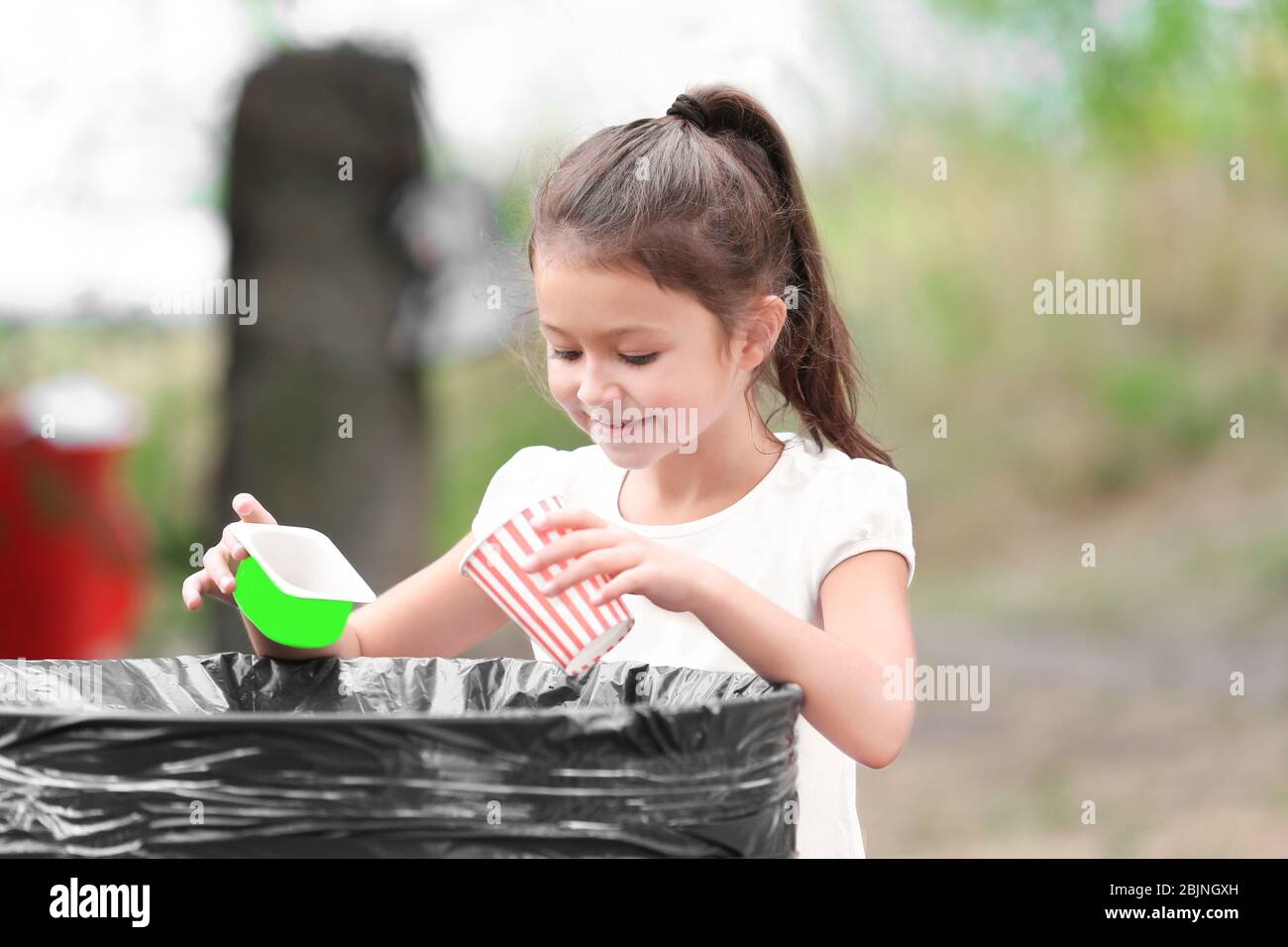 Little girl throwing garbage into litter bin outdoors Stock Photo