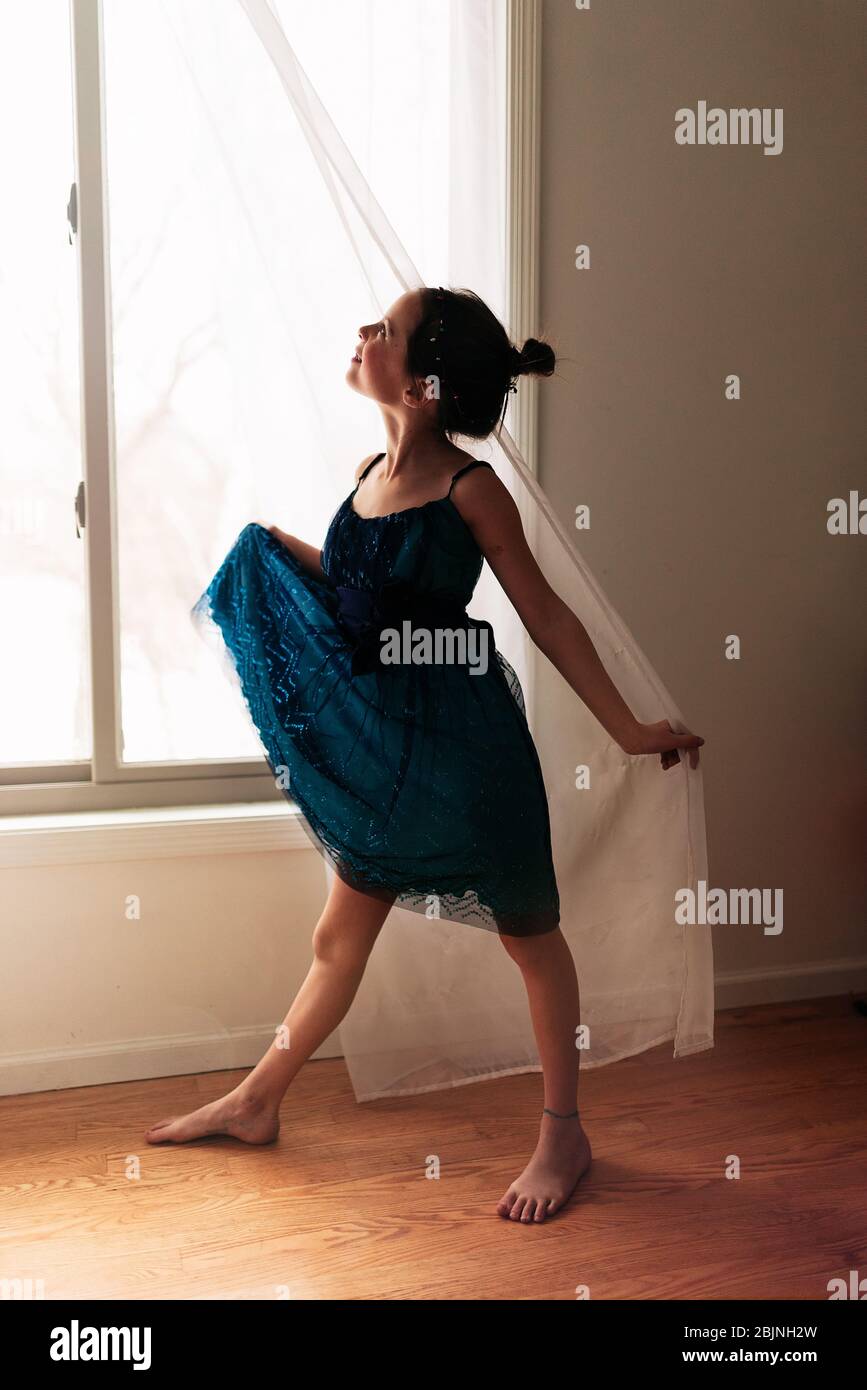 Portrait of a young girl standing by a window holding the curtain Stock Photo