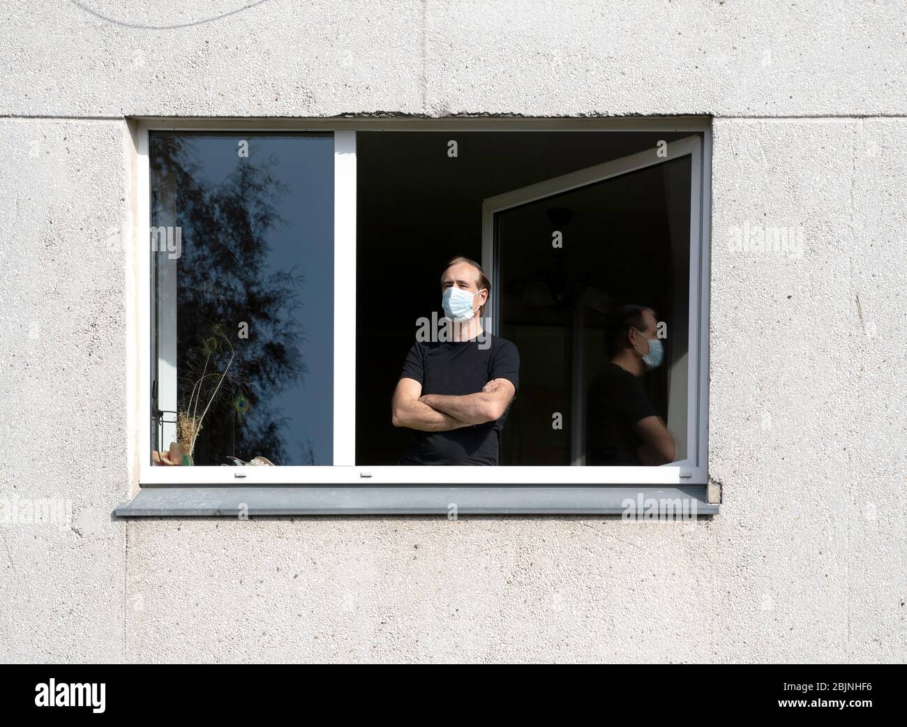 Man wearing a face mask looking out of a window, Lithuania Stock Photo