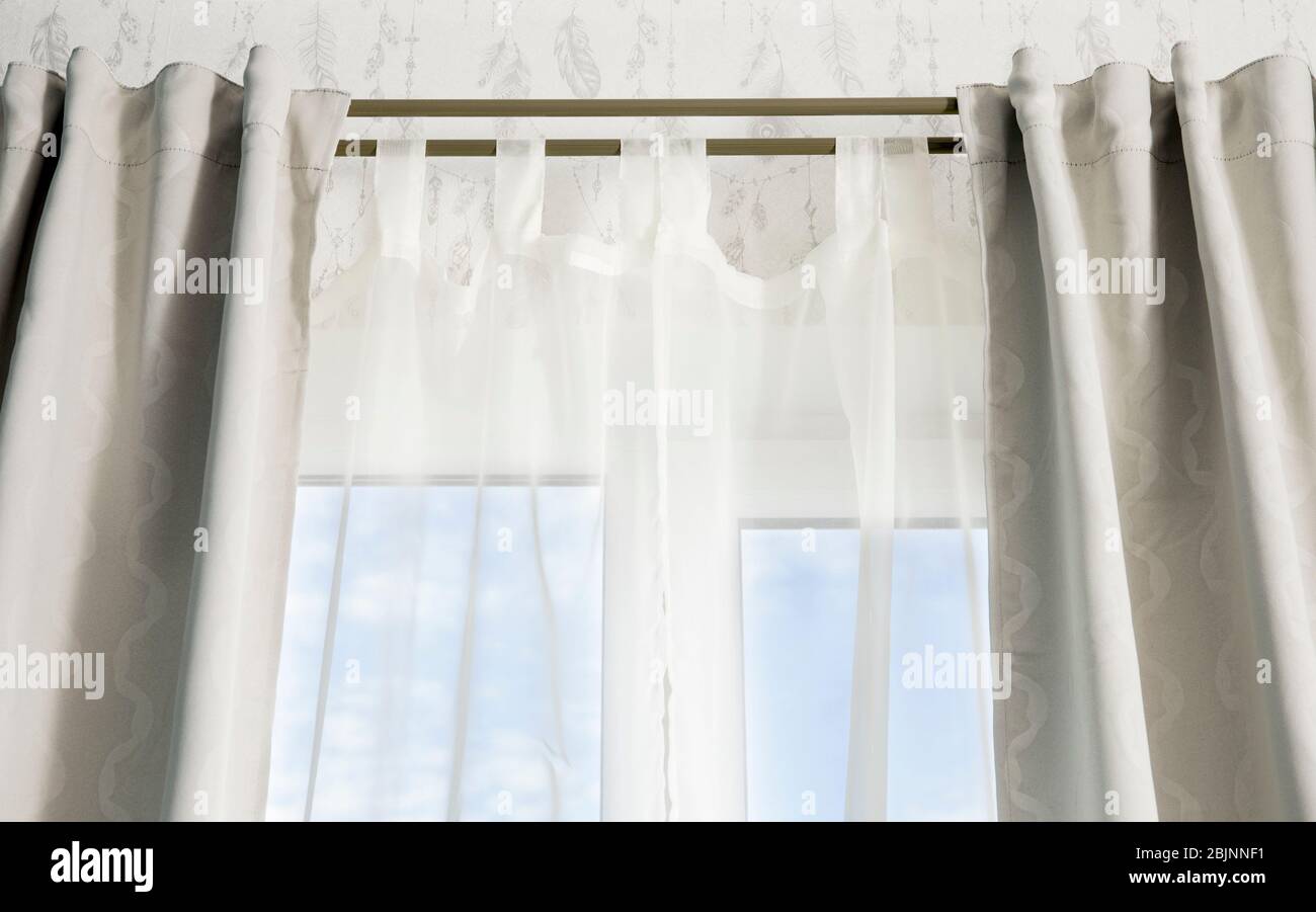 Double curtain rods for see through day curtain and room darkening night curtains. Hanging in front of a window with blue sky. Stock Photo