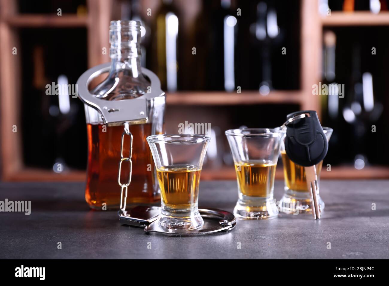 Glassware of alcohol with handcuffs and car key on table in bar. Don't ...