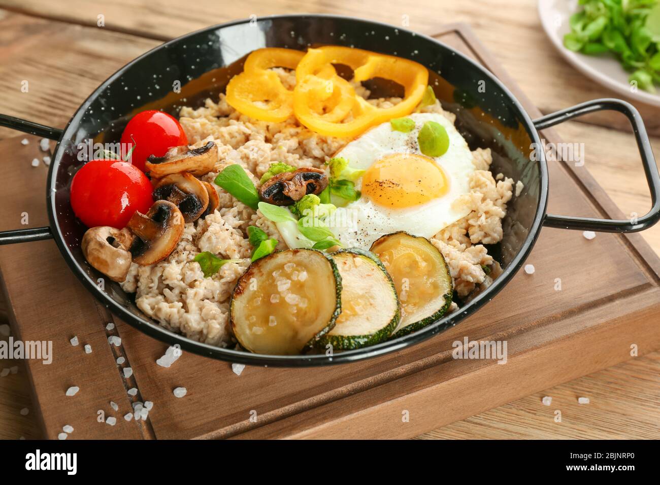 Frying egg with oatmeal, egg, mushrooms and vegetables on table Stock Photo