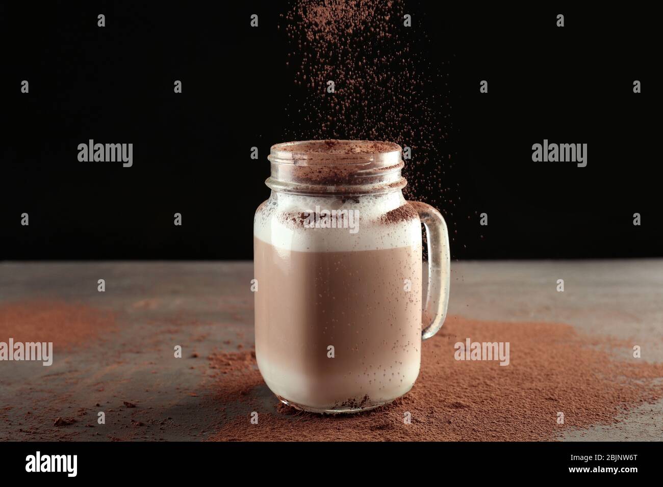 Pouring cinnamon powder into mason jar with latte macchiato on black