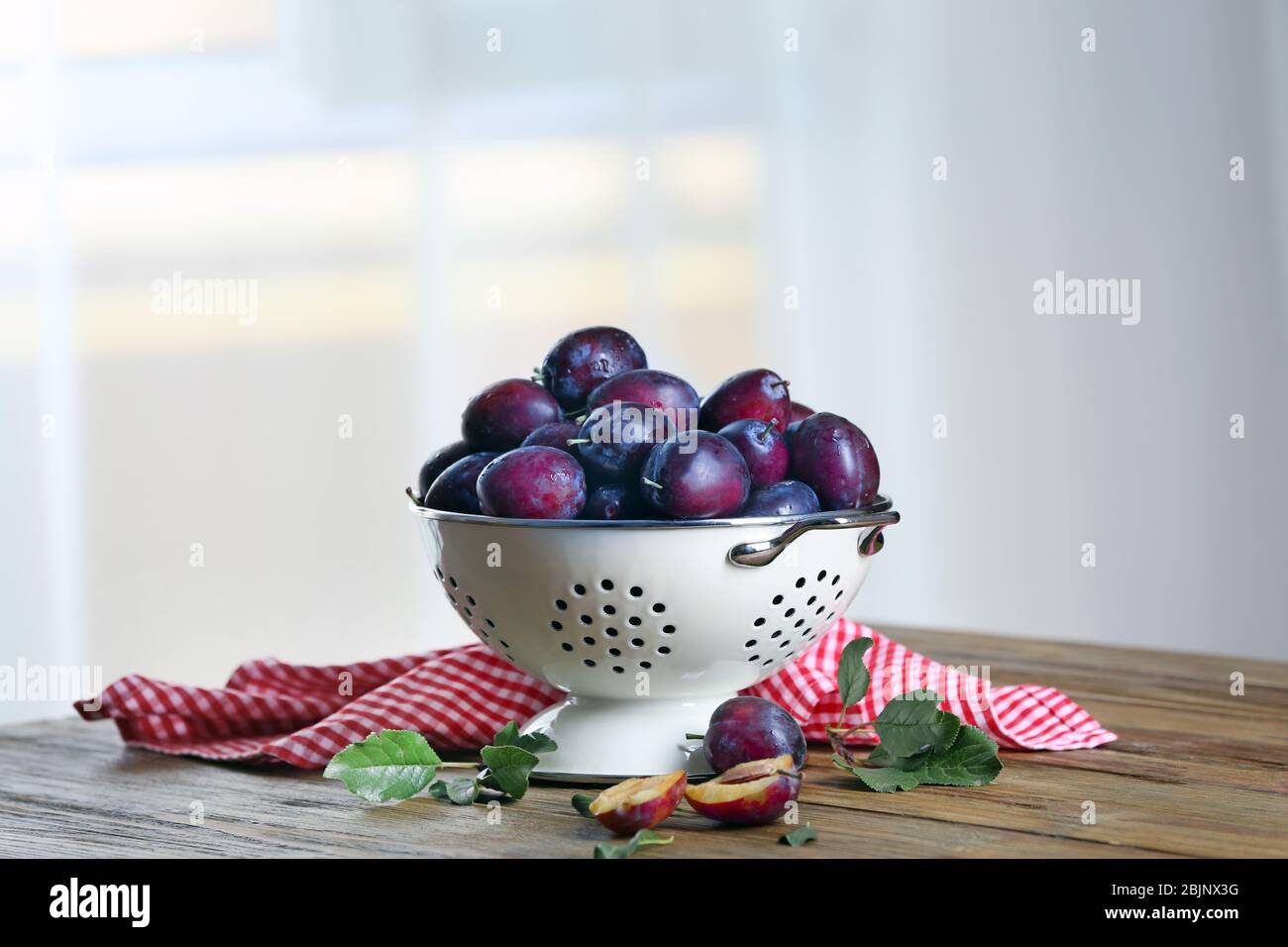 Fresh plums in colander on table Stock Photo