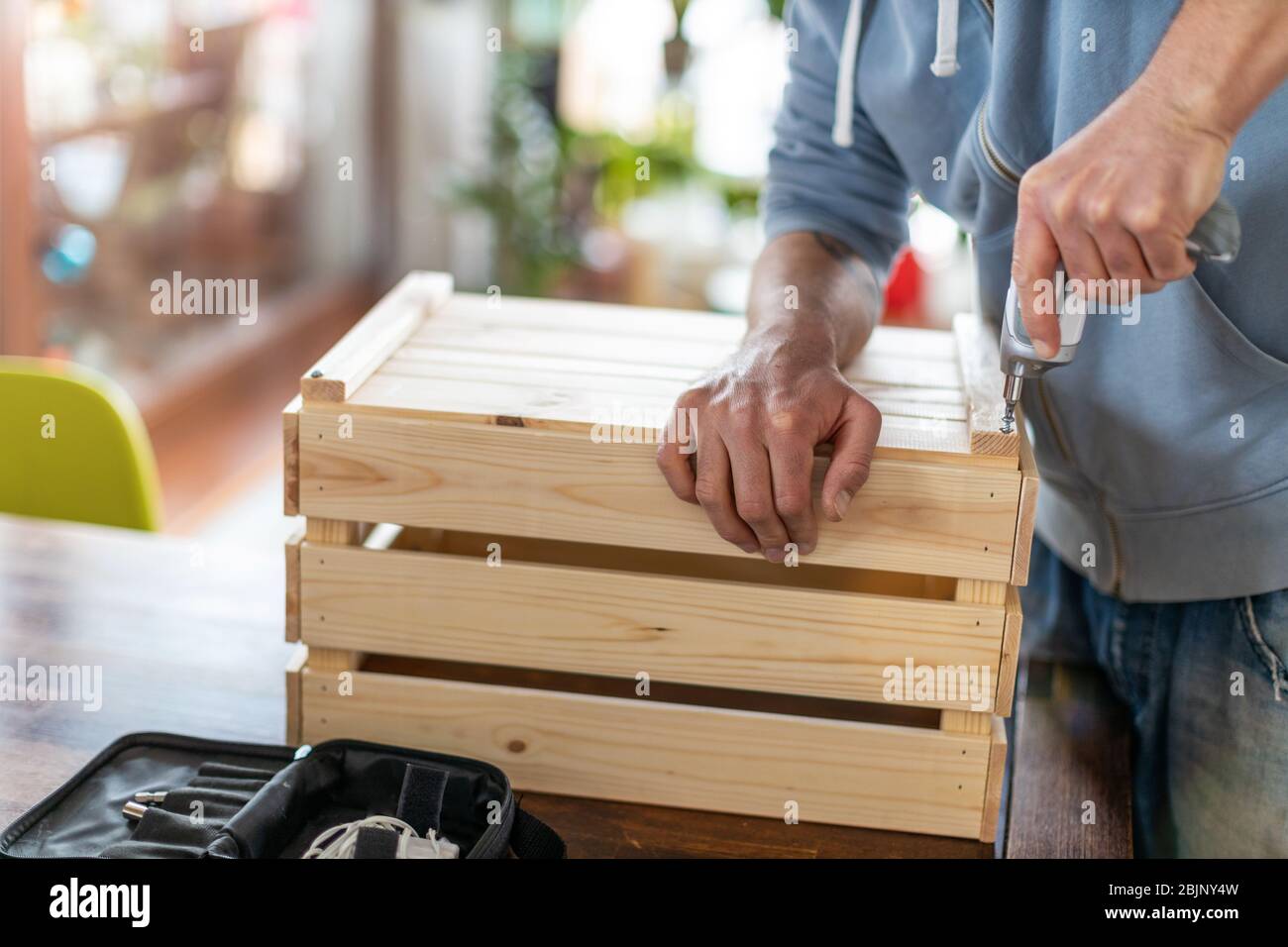 Man drilling wooden crate with power tool at home Stock Photo