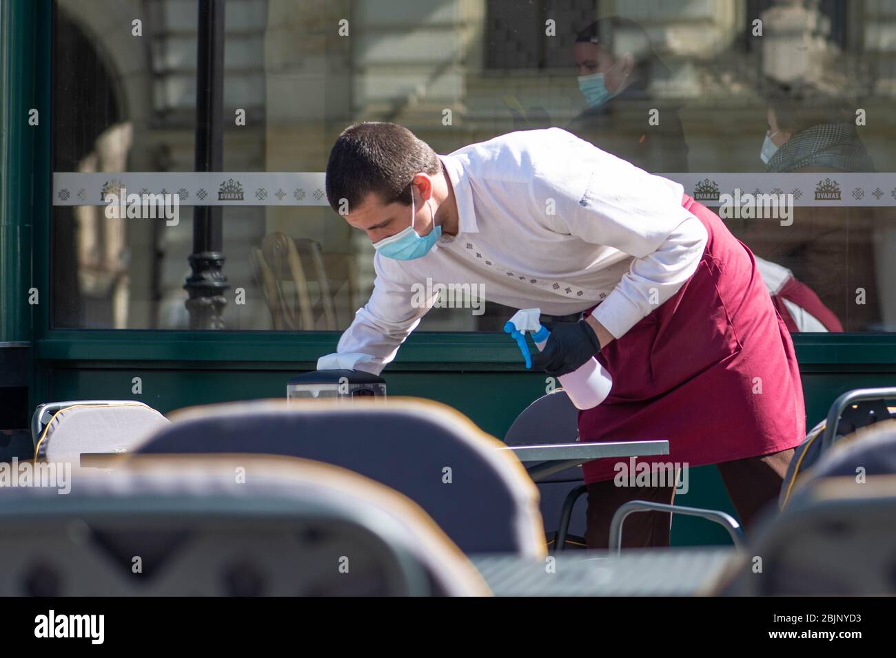 Waiter with a mask disinfects the table of an outdoor bar, café or restaurant, reopen after quarantine restrictions Stock Photo