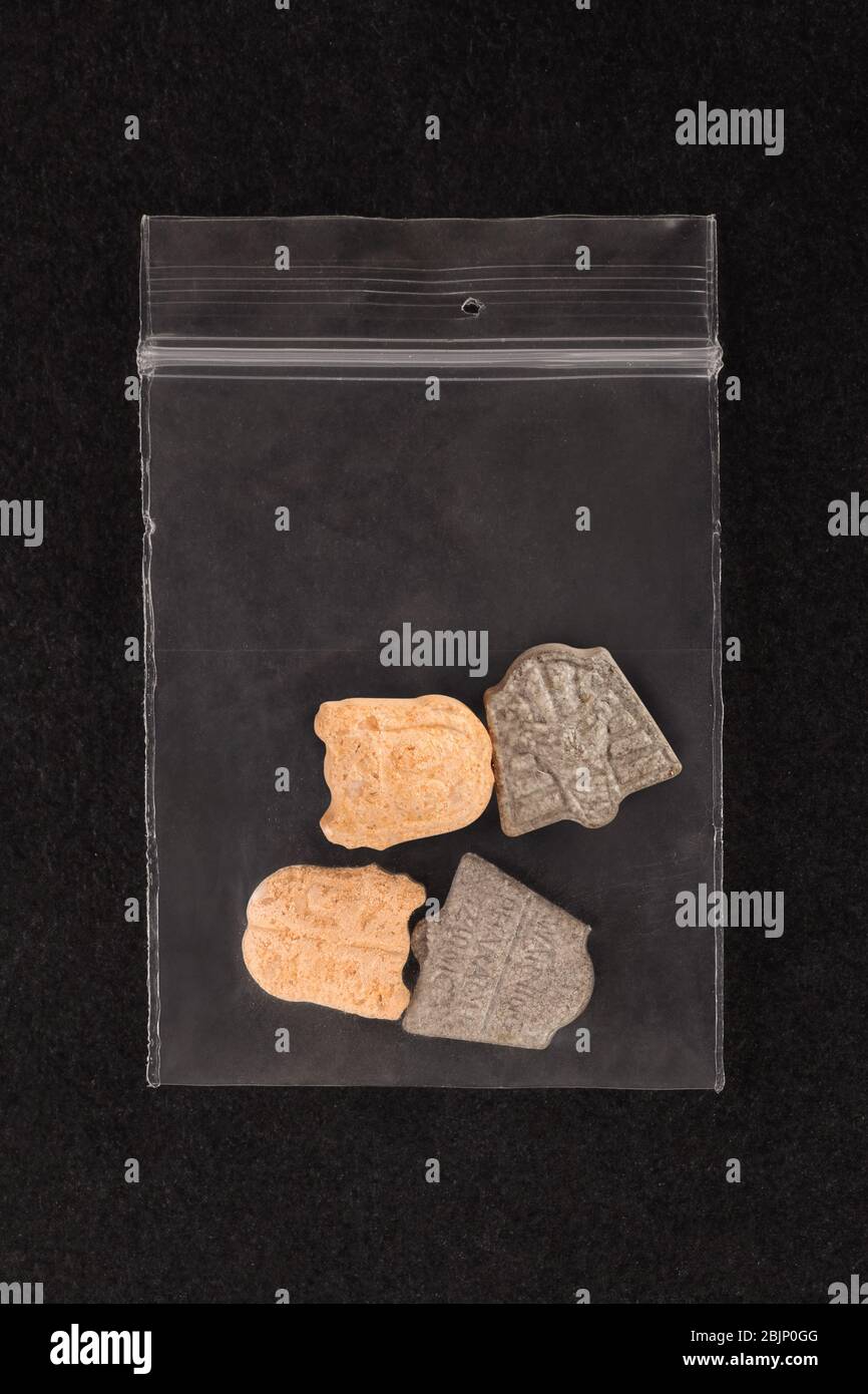 Ecstasy pills in plastic bag on black background from above. Stock Photo