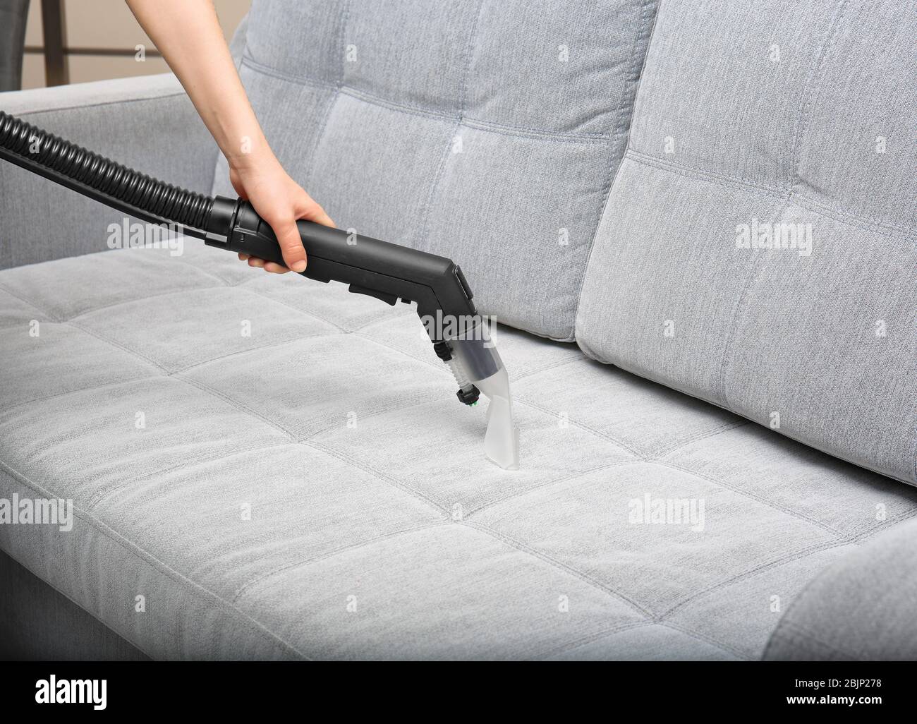 Male worker removing dirty stain from grey sofa with vacuum cleaner in room  Stock Photo - Alamy