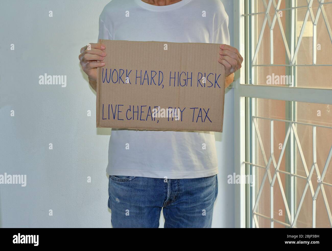 A worker holding cardboard sign read WORK HARD, HIGH RISK, LIVE CHEAP, PAY TAX, demonstration concept Stock Photo