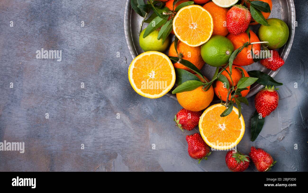 Assorted fruits. Different fruits on a gray background, the whole surface is covered with citrus fruits, pomegranates, apples, grapes, strawberries. Top view. Copy space. Stock Photo
