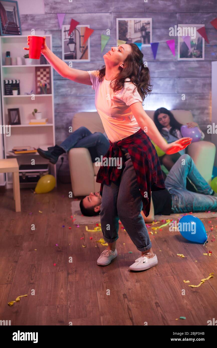 Young woman dancing alone at friends party. Group of friend lying on