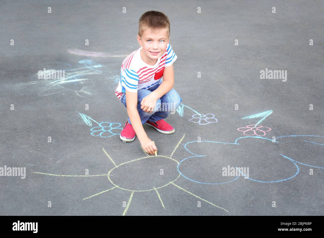 Cute little boy drawing with chalk on asphalt Stock Photo - Alamy