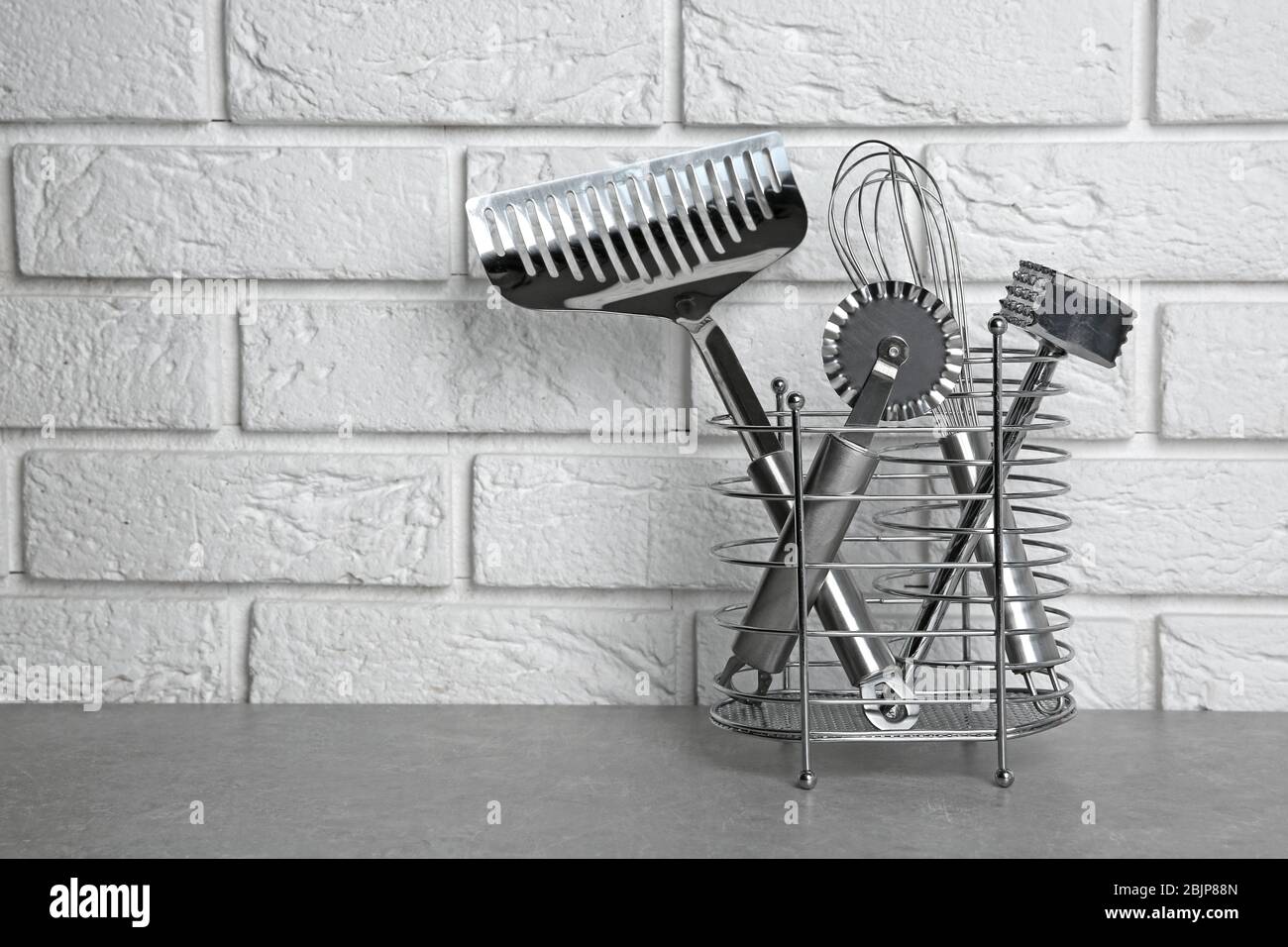 Stand with kitchen utensils on table against white wall Stock Photo - Alamy